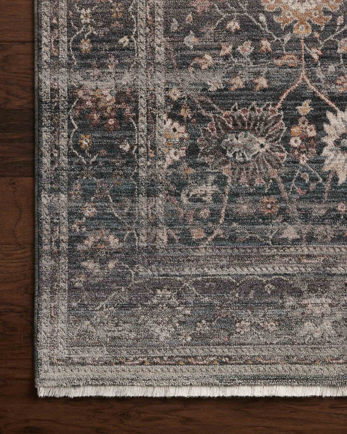 Corner detail of ink-toned area rug with distressed pattern and short fringe
