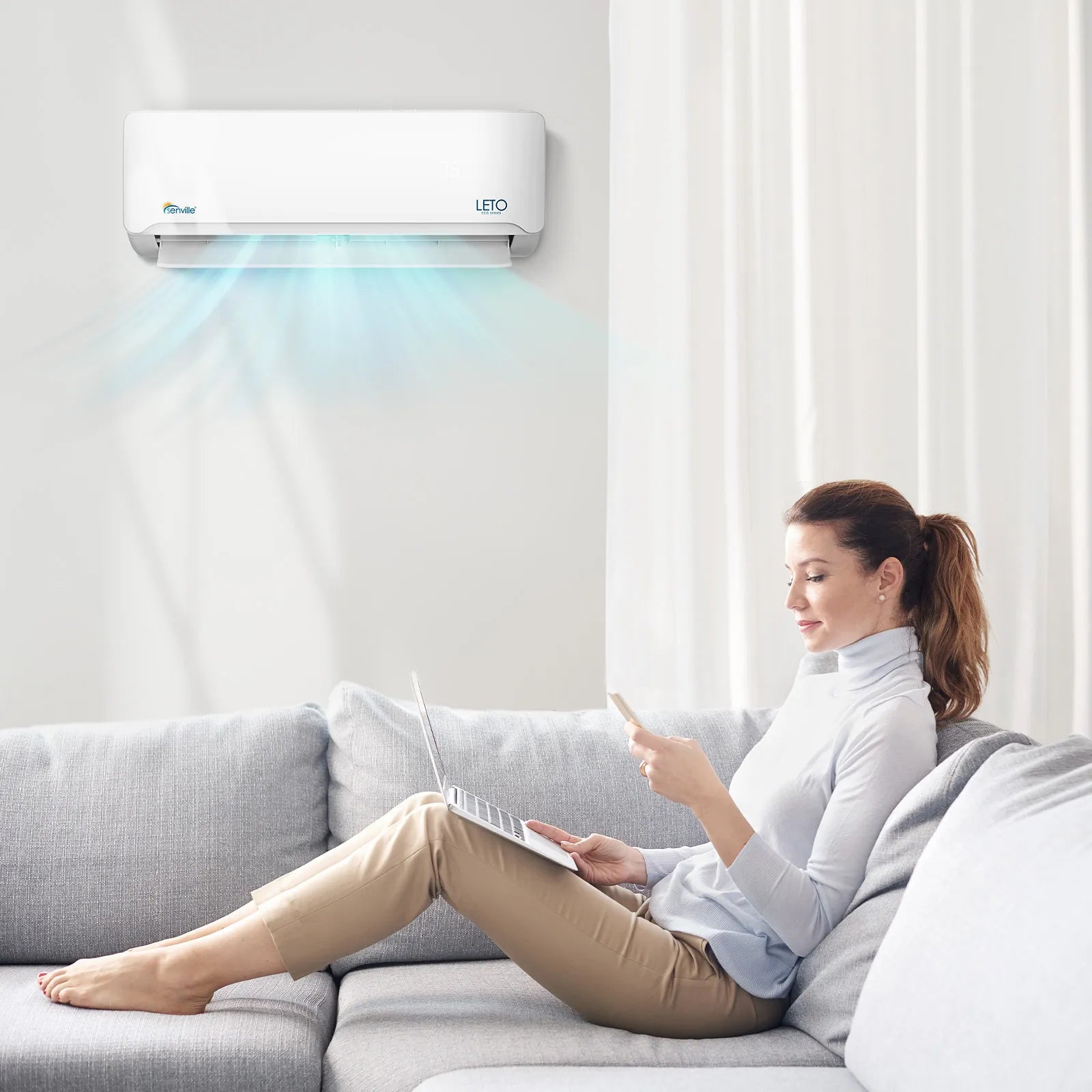 Wall-mounted mini split indoor unit above couch, white housing with front vent strip