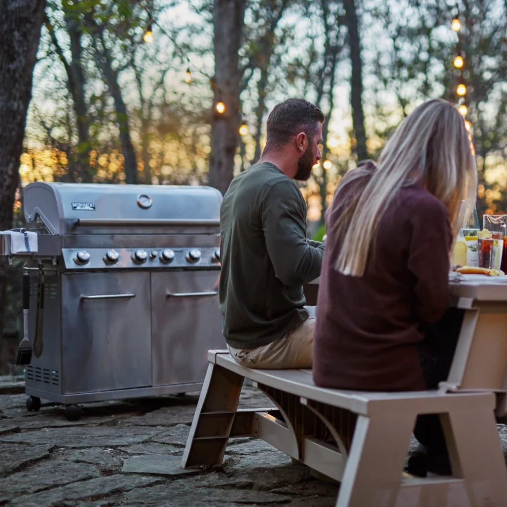 Stainless steel propane gas grill with control knobs and diners seated nearby
