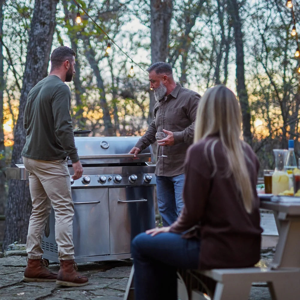 Stainless steel propane gas grill with open cooking area surrounded by diners