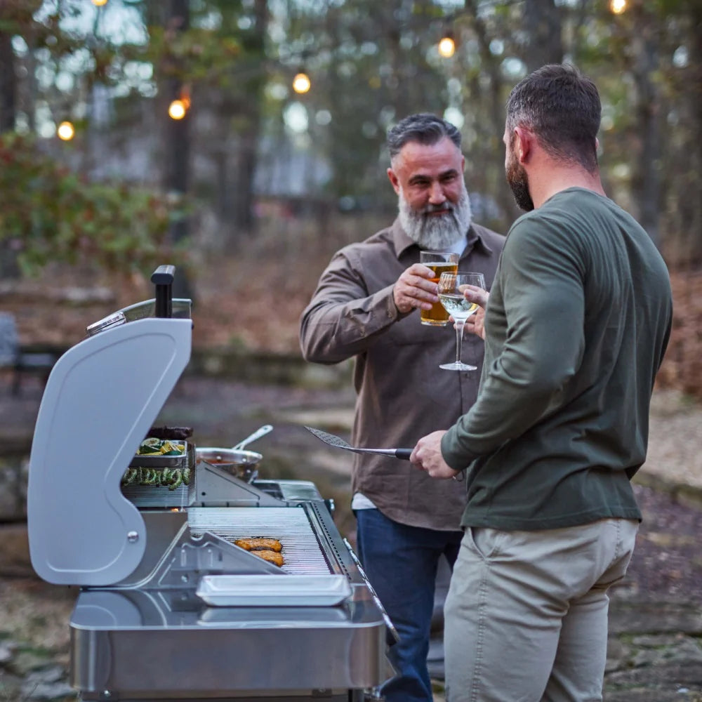 Stainless steel propane gas grill with lid open, side shelf, and cooking grate in use