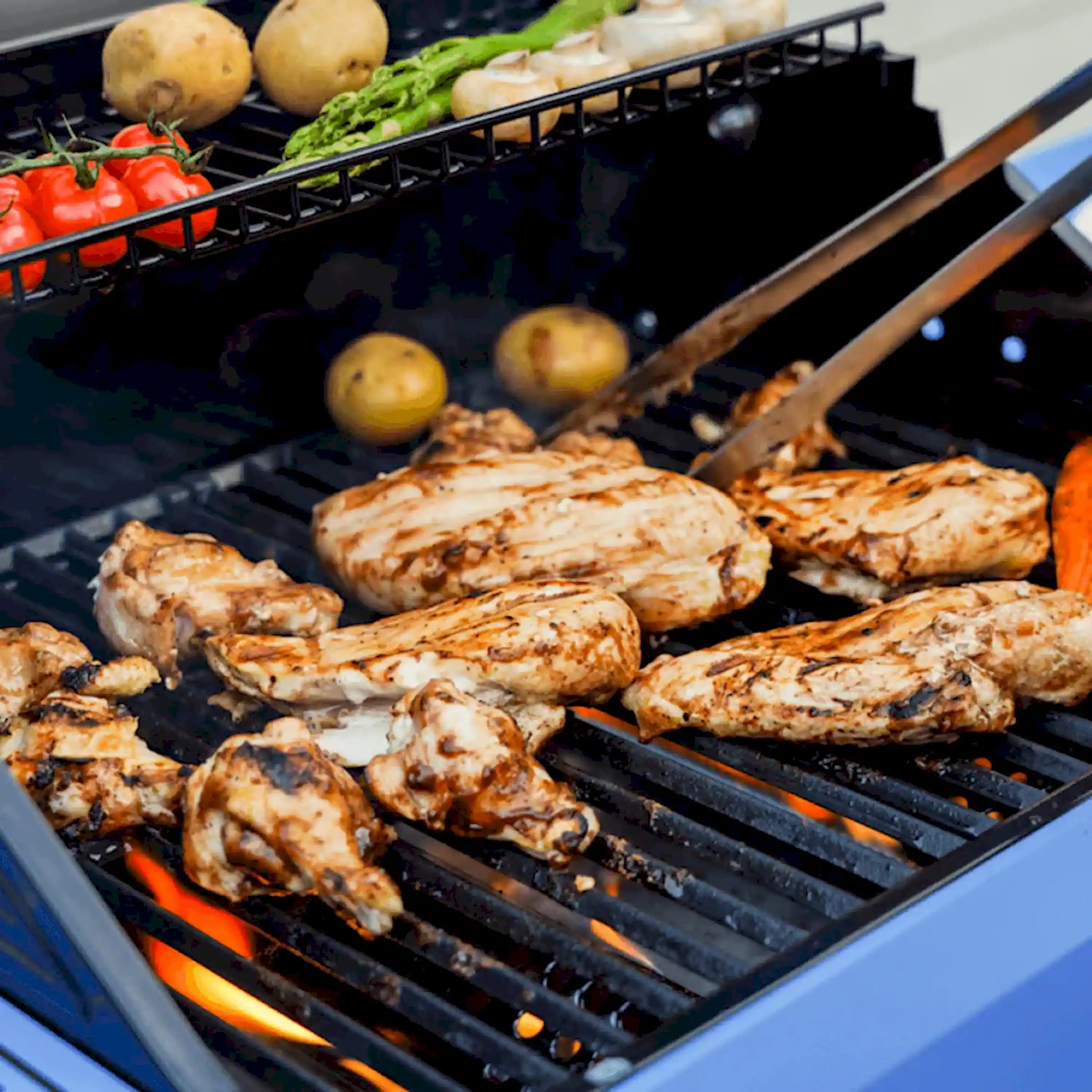 Propane grill with dark grates and chicken pieces cooking alongside potatoes