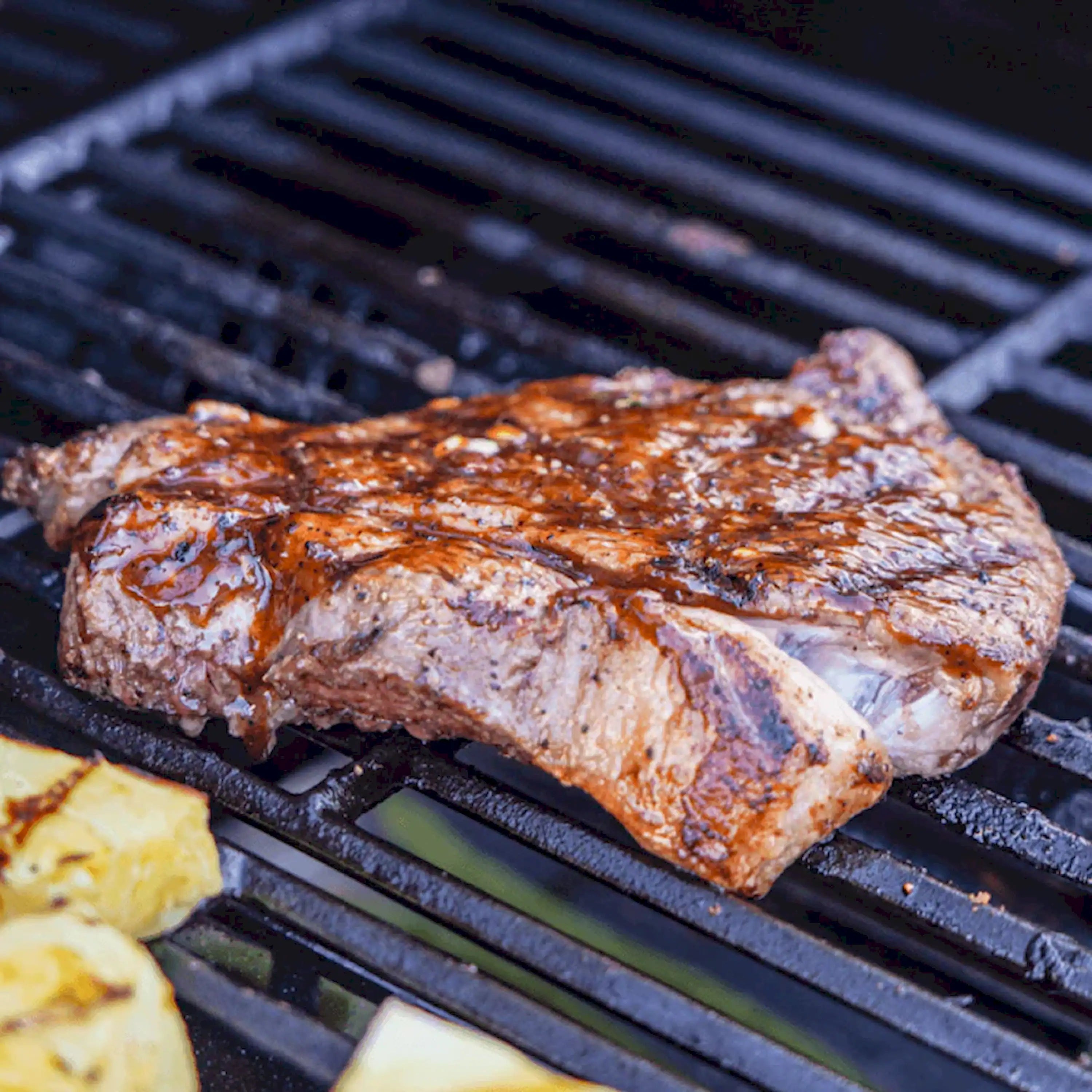 Propane grill cooking grate with seared steak and browned char marks