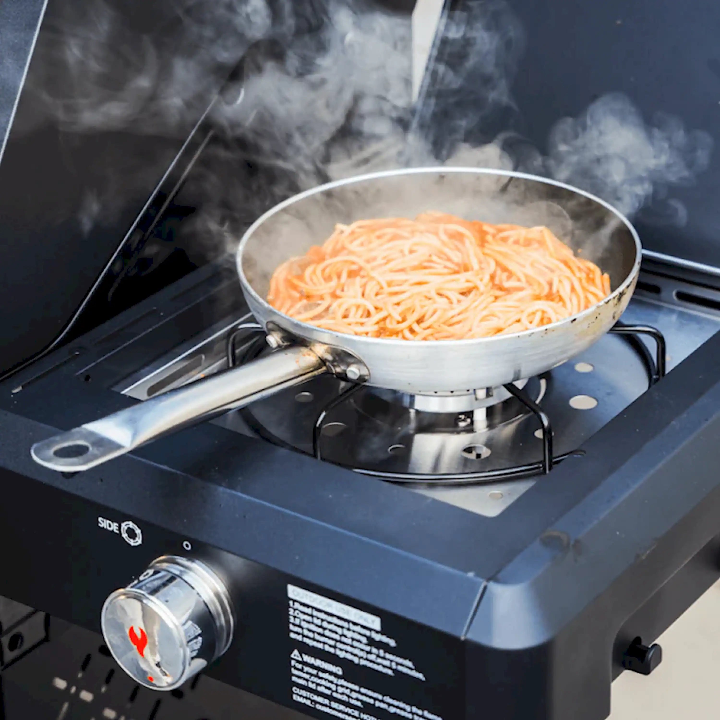 Black propane grill side burner with a steaming pot of spaghetti