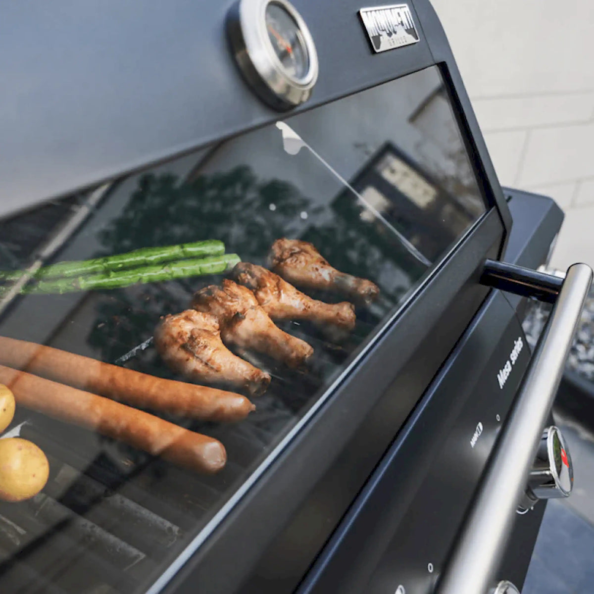 Black propane gas grill with lid open, cooking sausages and vegetables on grates