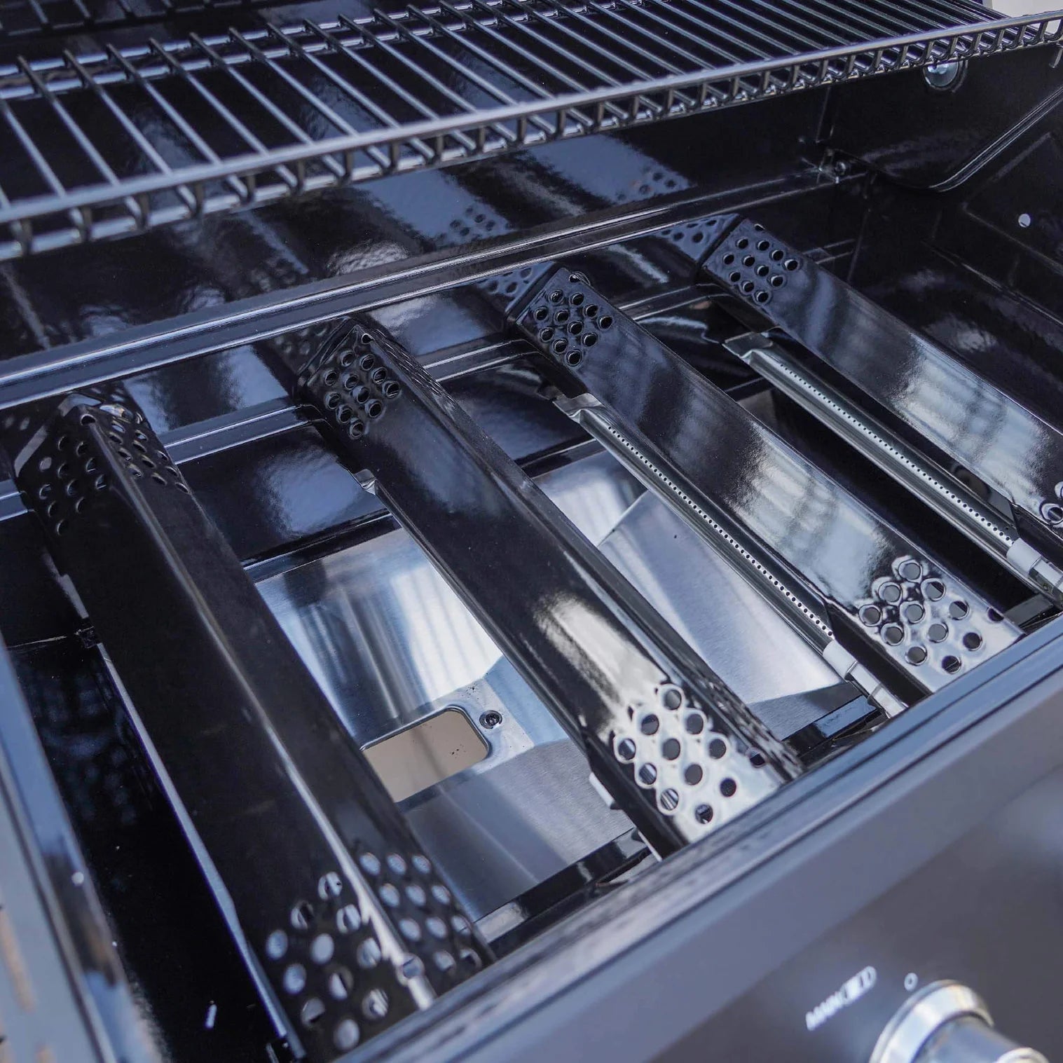 Open stainless steel grill with cooking grate above and perforated heat shield plates below