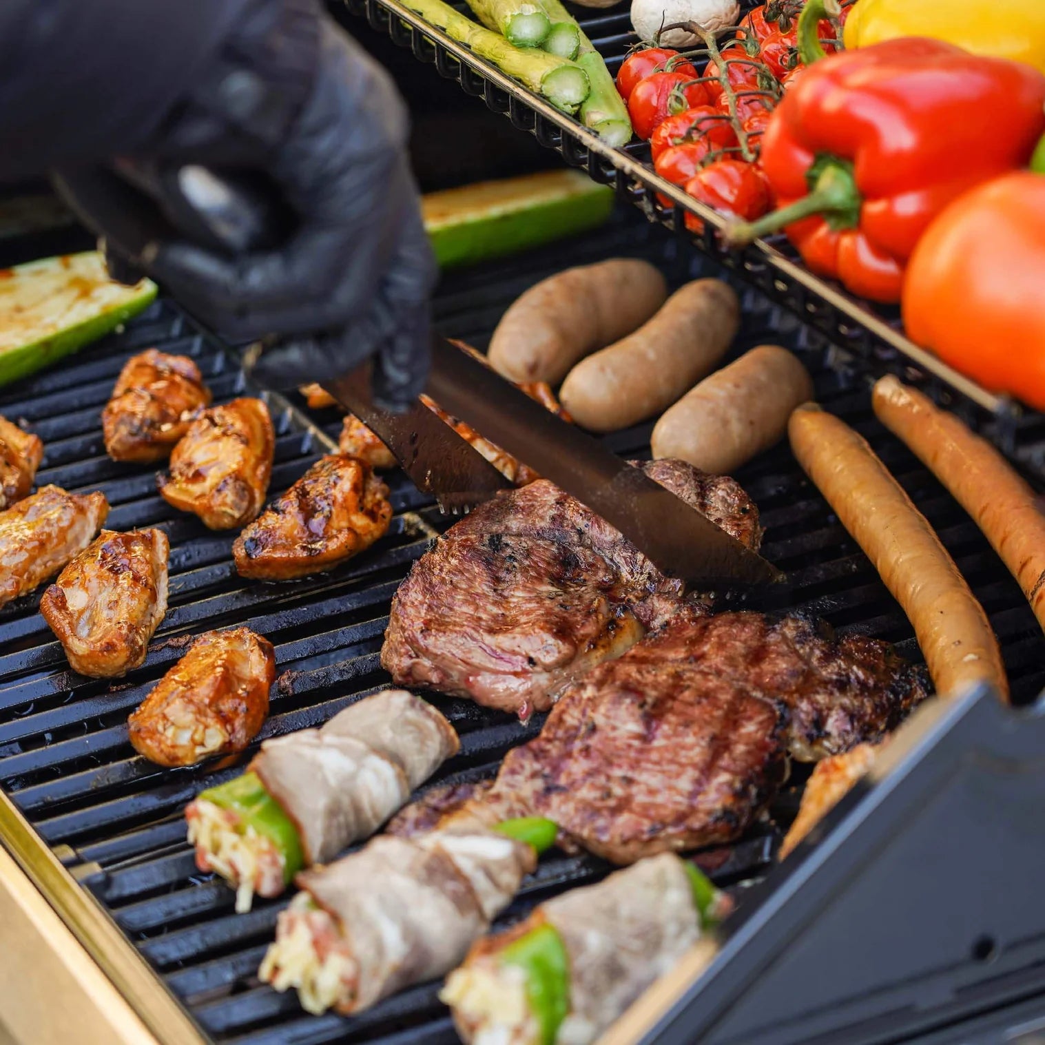 Assorted grilled foods on dark grill grates, including sausages, peppers, and steaks