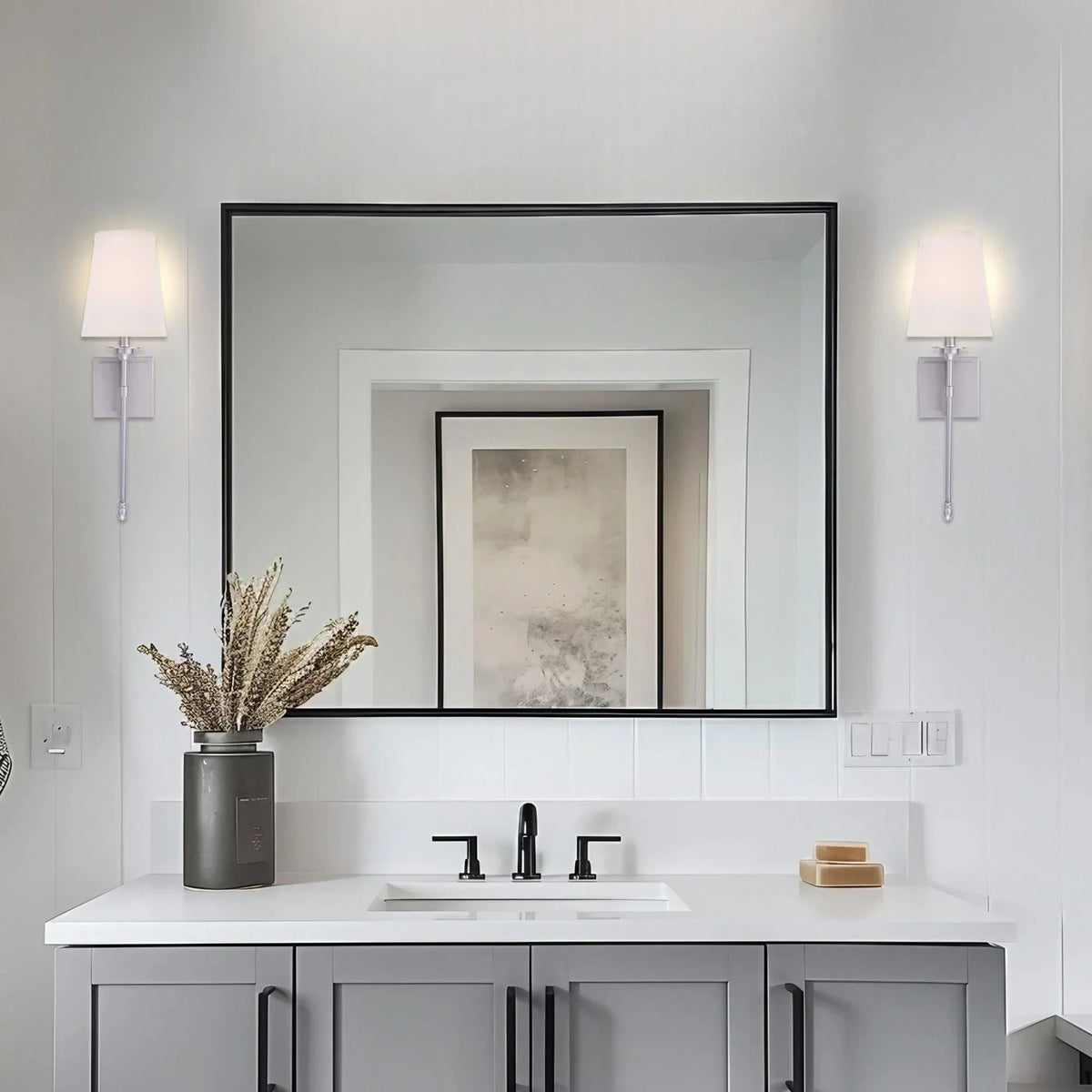 Black 1-light wall sconce with white fabric shade mounted beside mirror