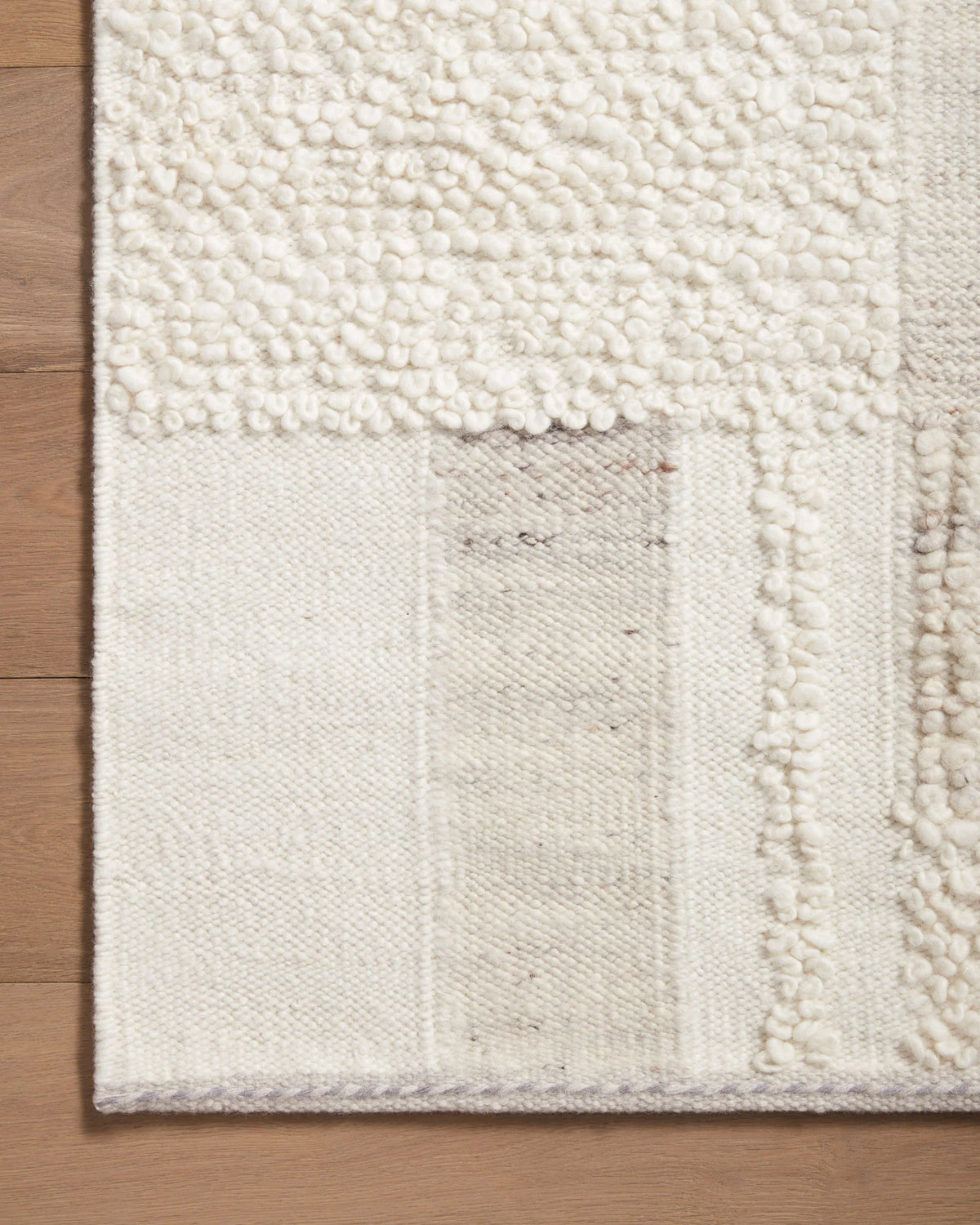 Ivory area rug corner with loop pile texture and subtle pebble-toned patch