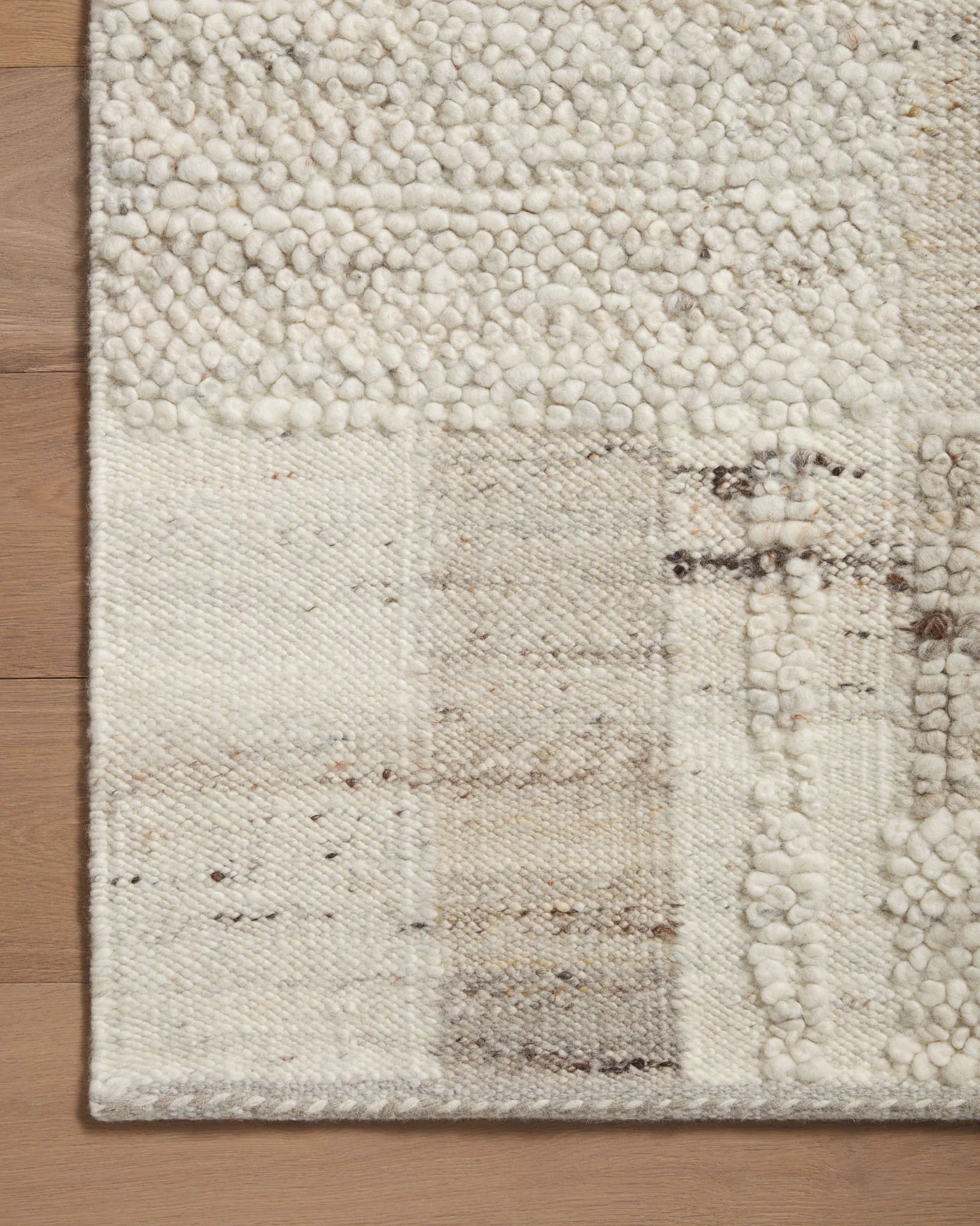 Natural area rug with looped texture, geometric patchwork and stone-gray corner edge