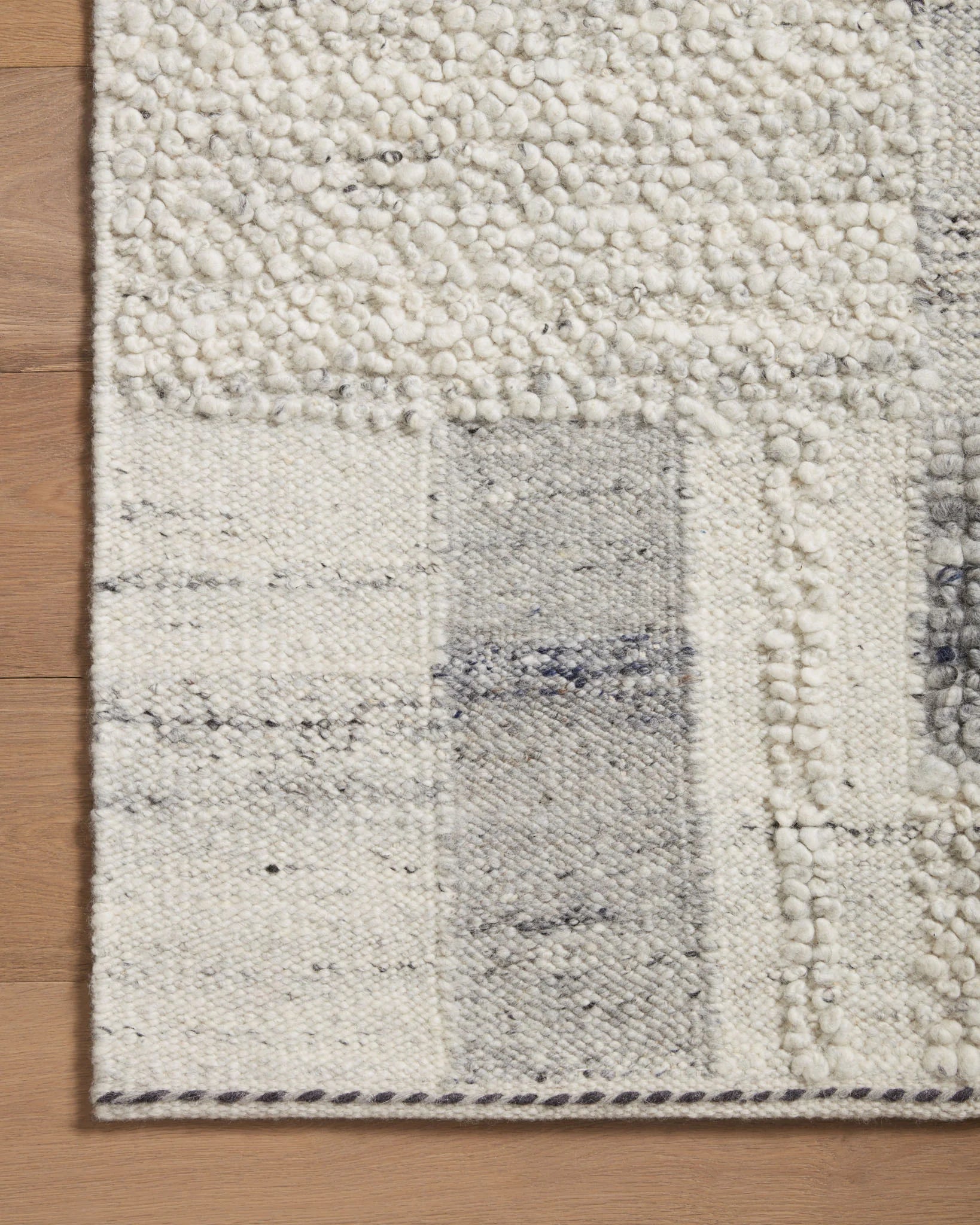 Textured accent rug close-up with mist base and slate-gray squares, bound edge