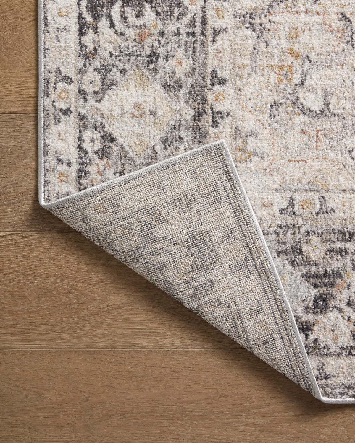 Abstract area rug corner lifted, showing low-texture pile and gray pattern