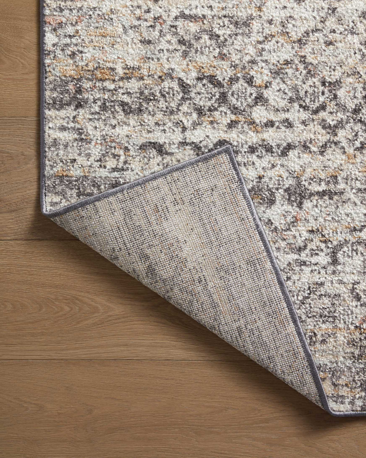 Gray area rug corner lifted to show reverse side and woven texture