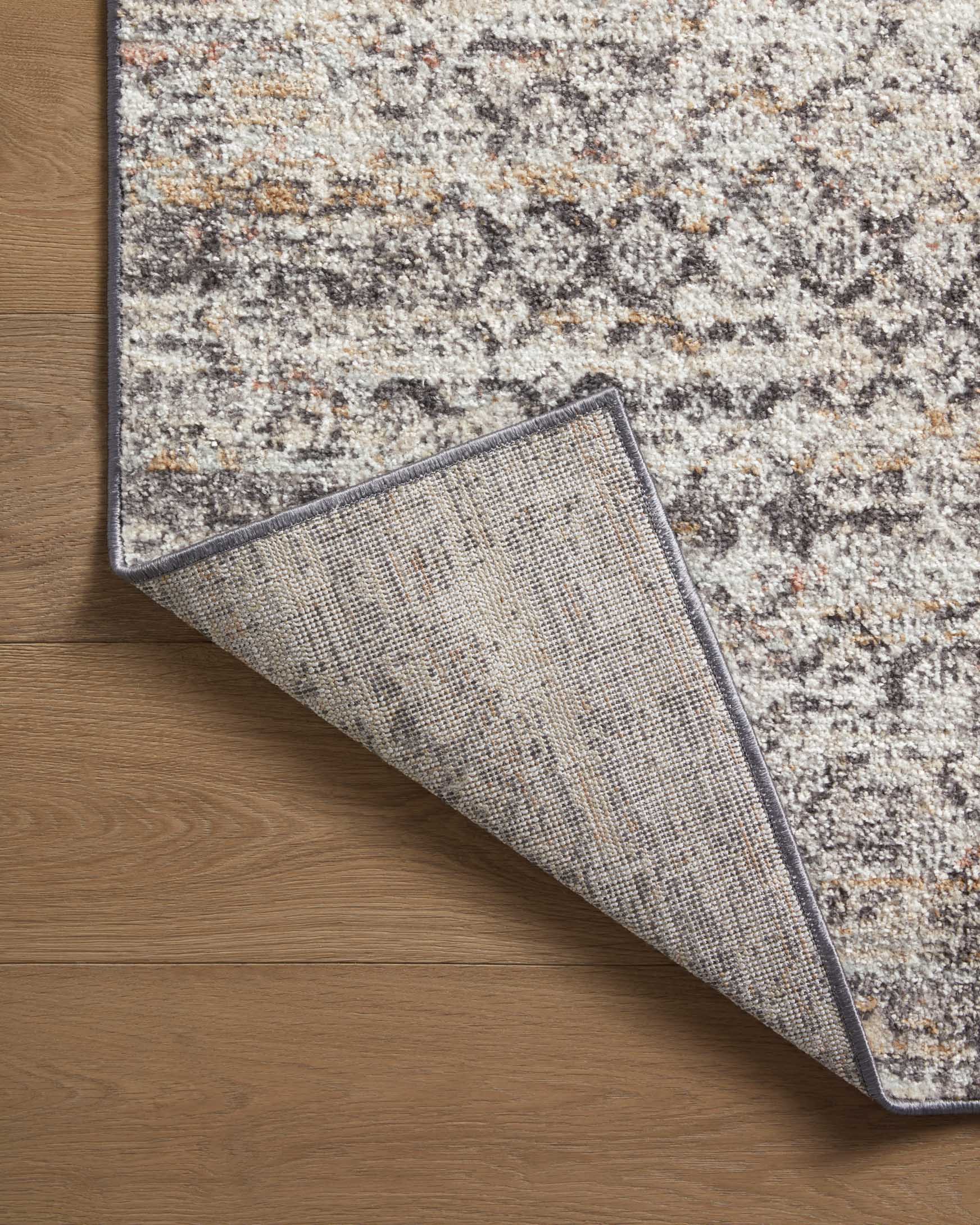 Gray area rug corner with visible underside weave detail and dark edge binding