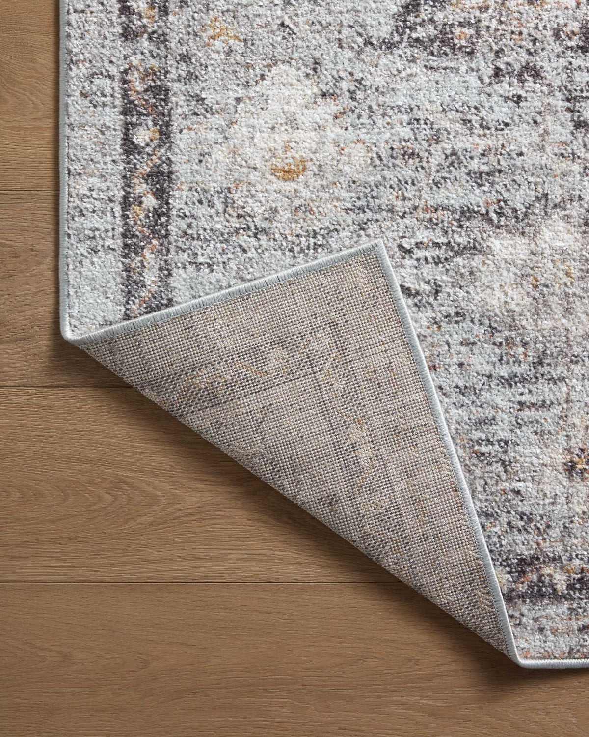 Sky and gold area rug edge folded back, showing woven texture on light gray backing