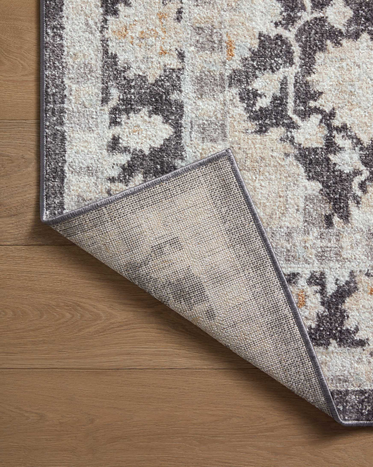 Charcoal and natural area rug rolled back to show backing texture and pile.