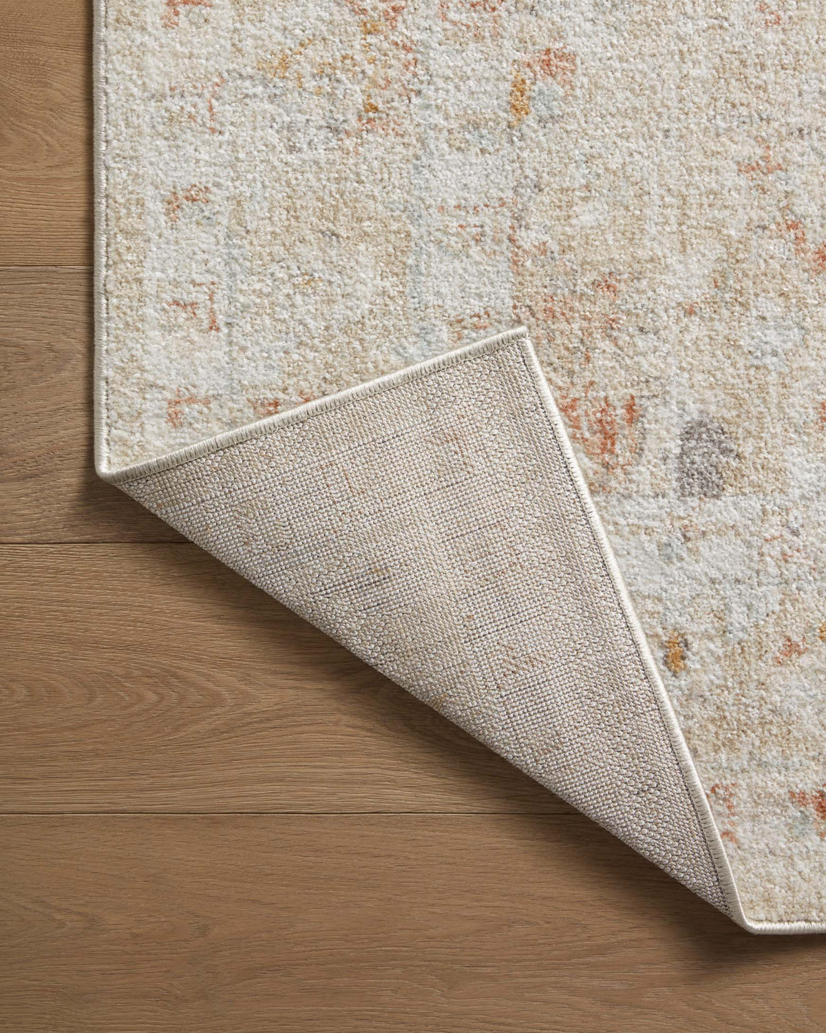 Area rug corner folded back, textured beige surface with orange-rust distressing