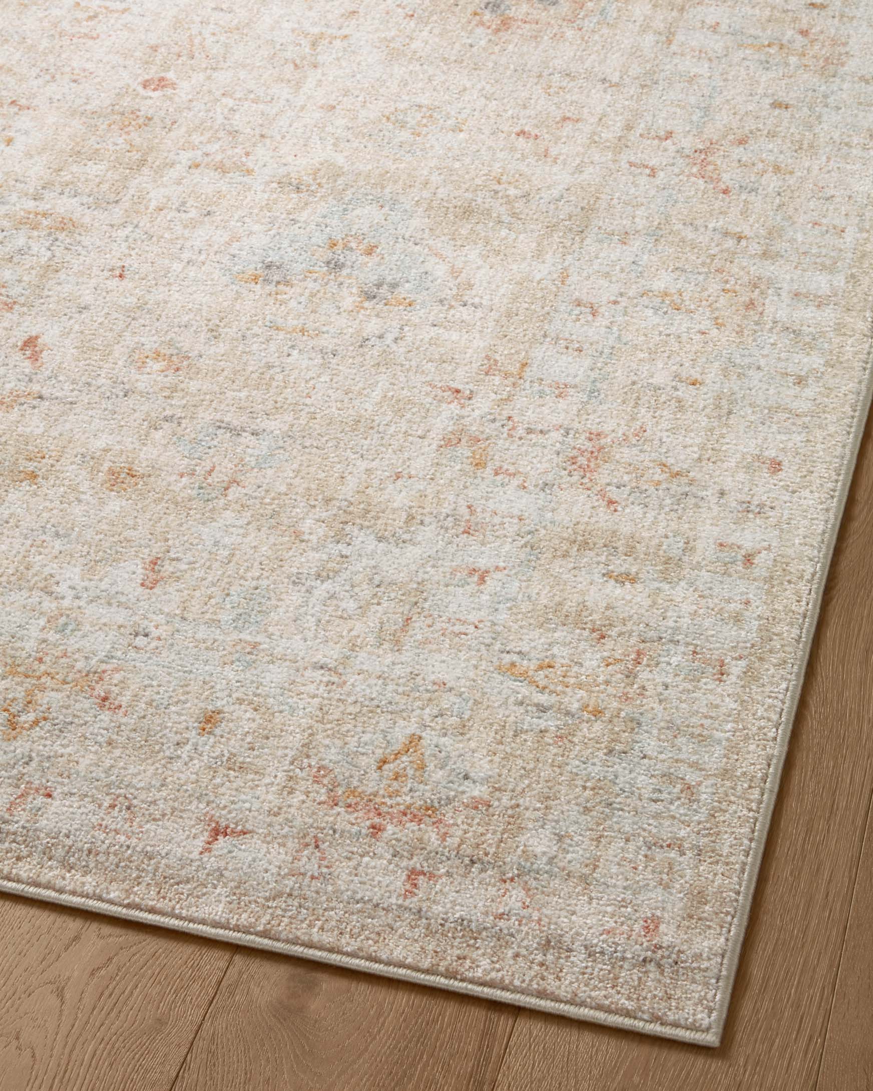 Sand rug corner close-up with distressed mottled pattern and rust-orange and light blue specks