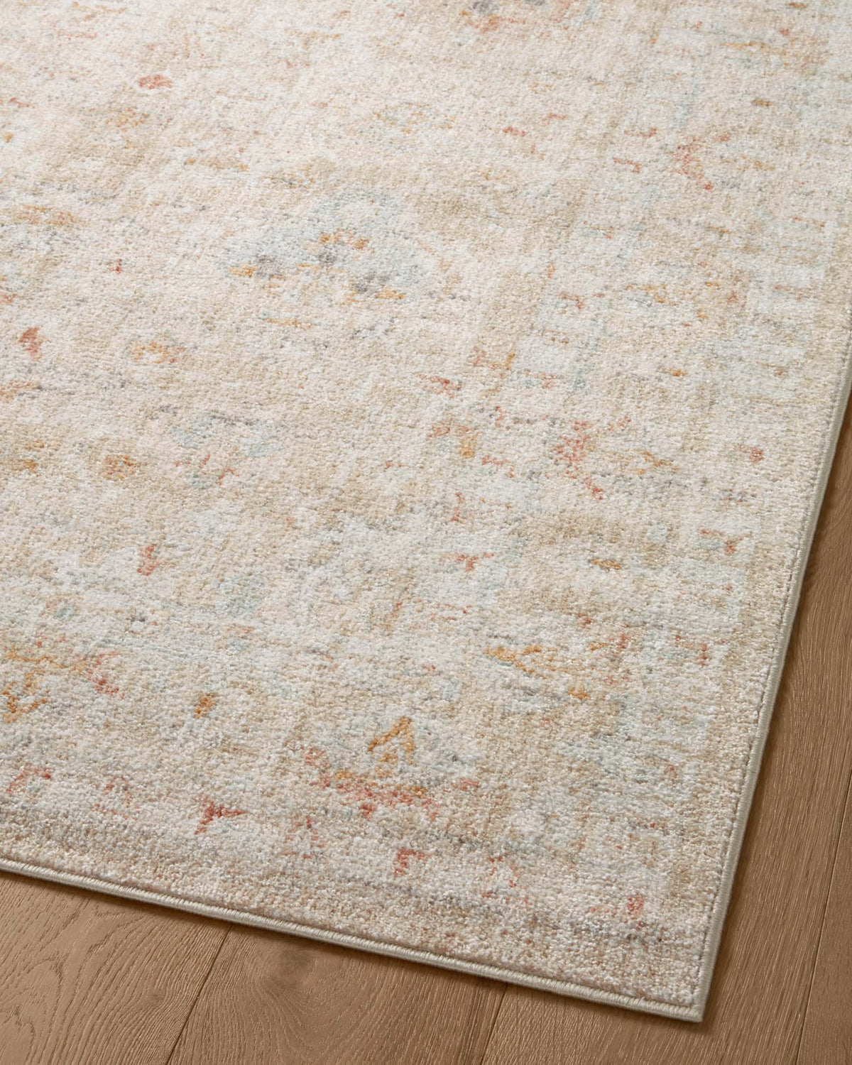 Close-up of light beige area rug with scattered orange and gray distressed marks