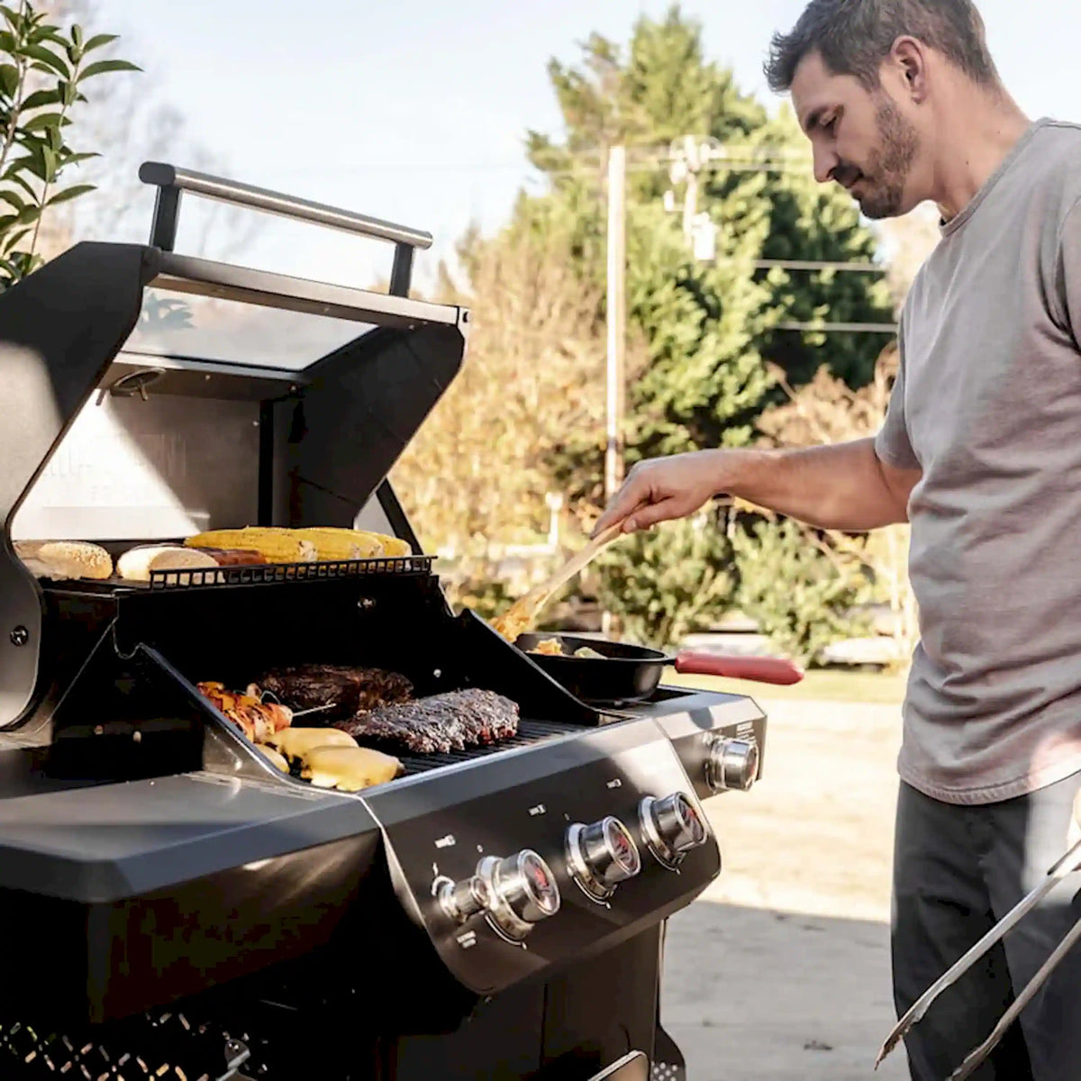 Black propane grill with lid open, cooking burgers and meat; control knobs visible