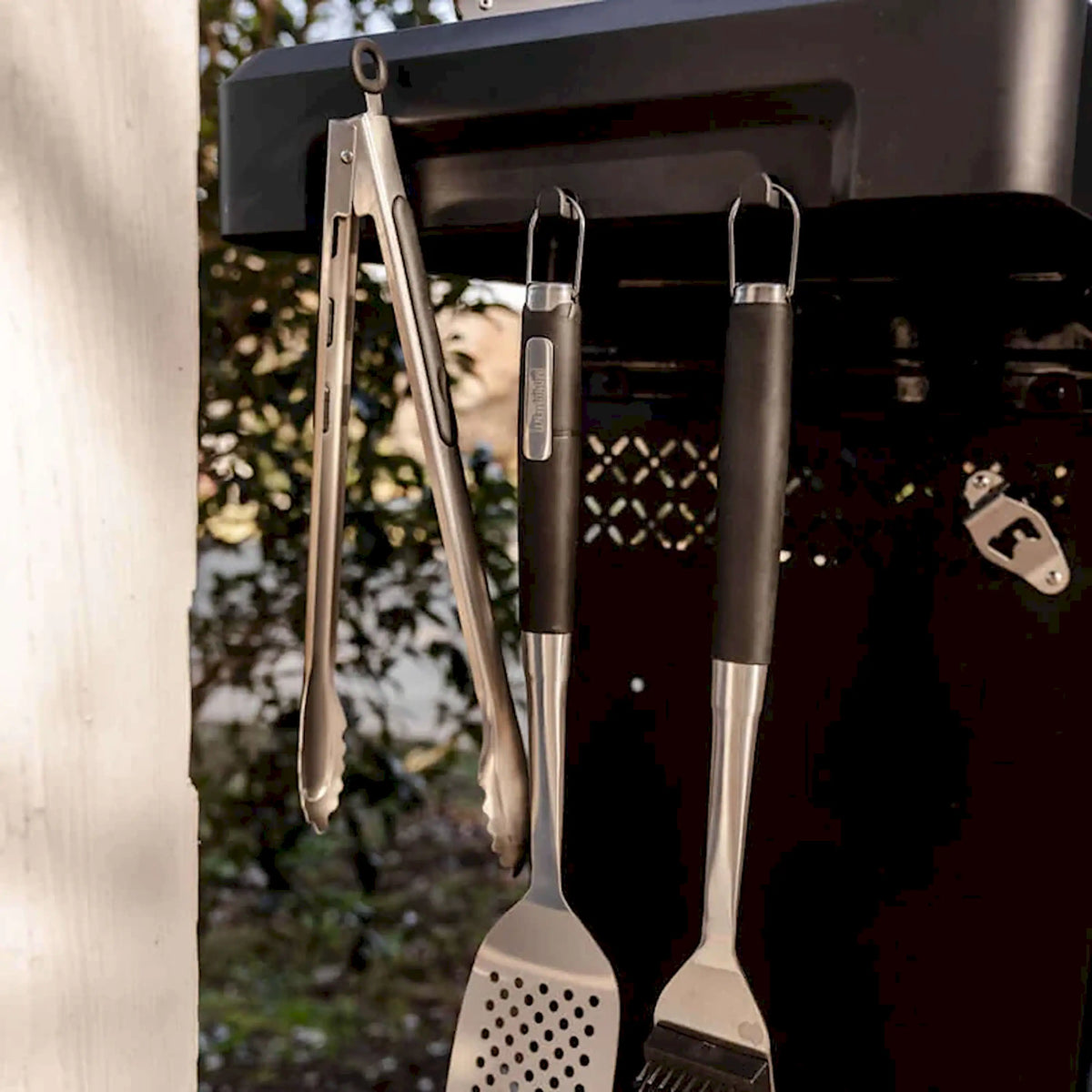 Black gas grill with two stainless grilling tools hanging on side