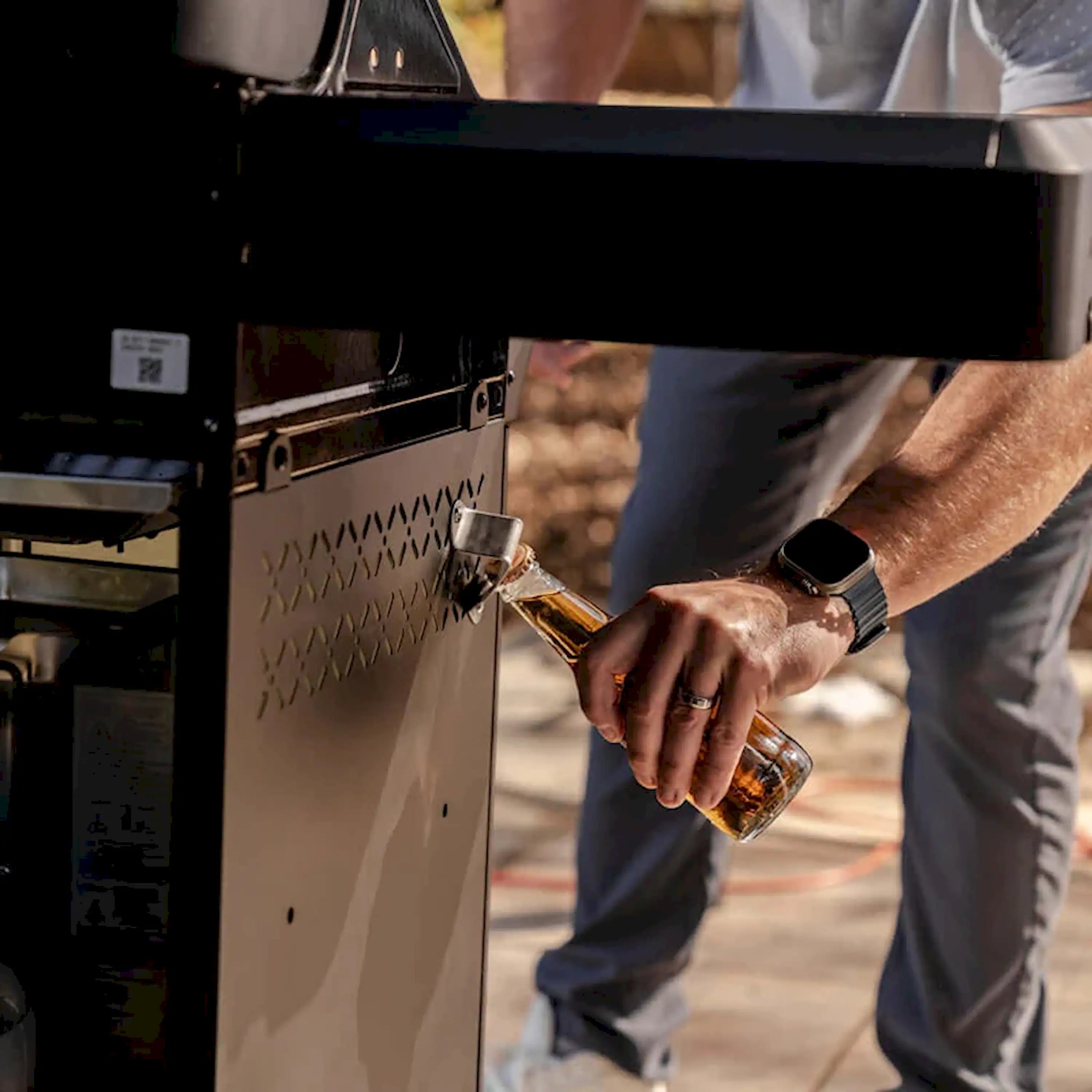 Man lighting a black propane grill with a hand control tool near the side panel