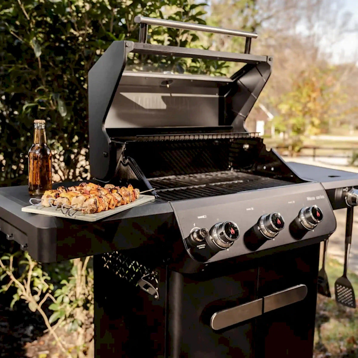 Black propane gas grill with lid open, shrimp grilling over wire grates