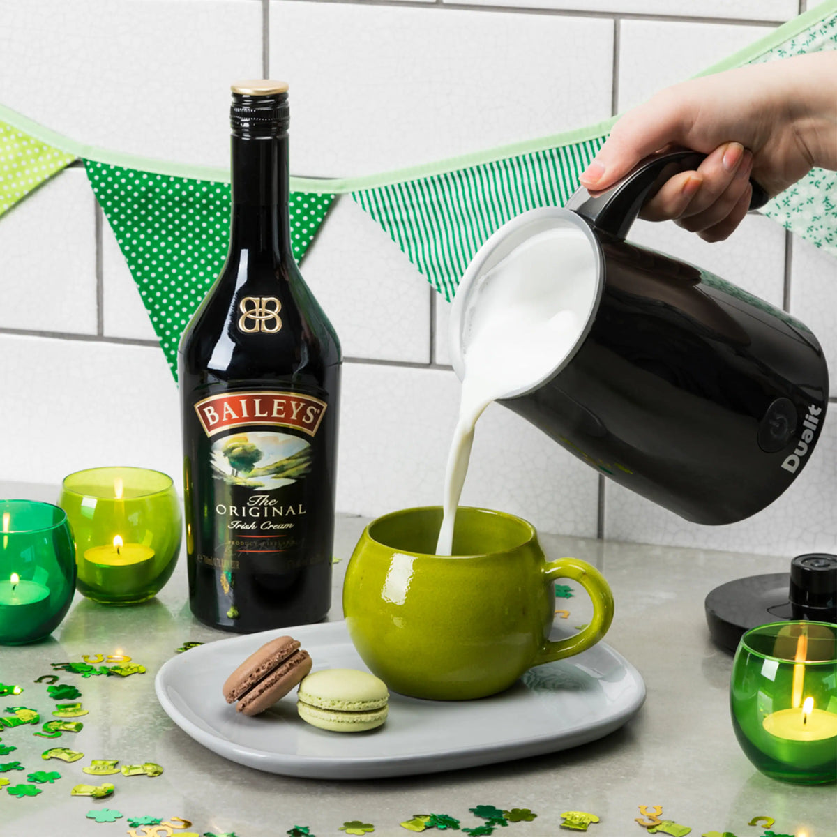 Dualit black milk frother pouring into a green mug beside plates and candles