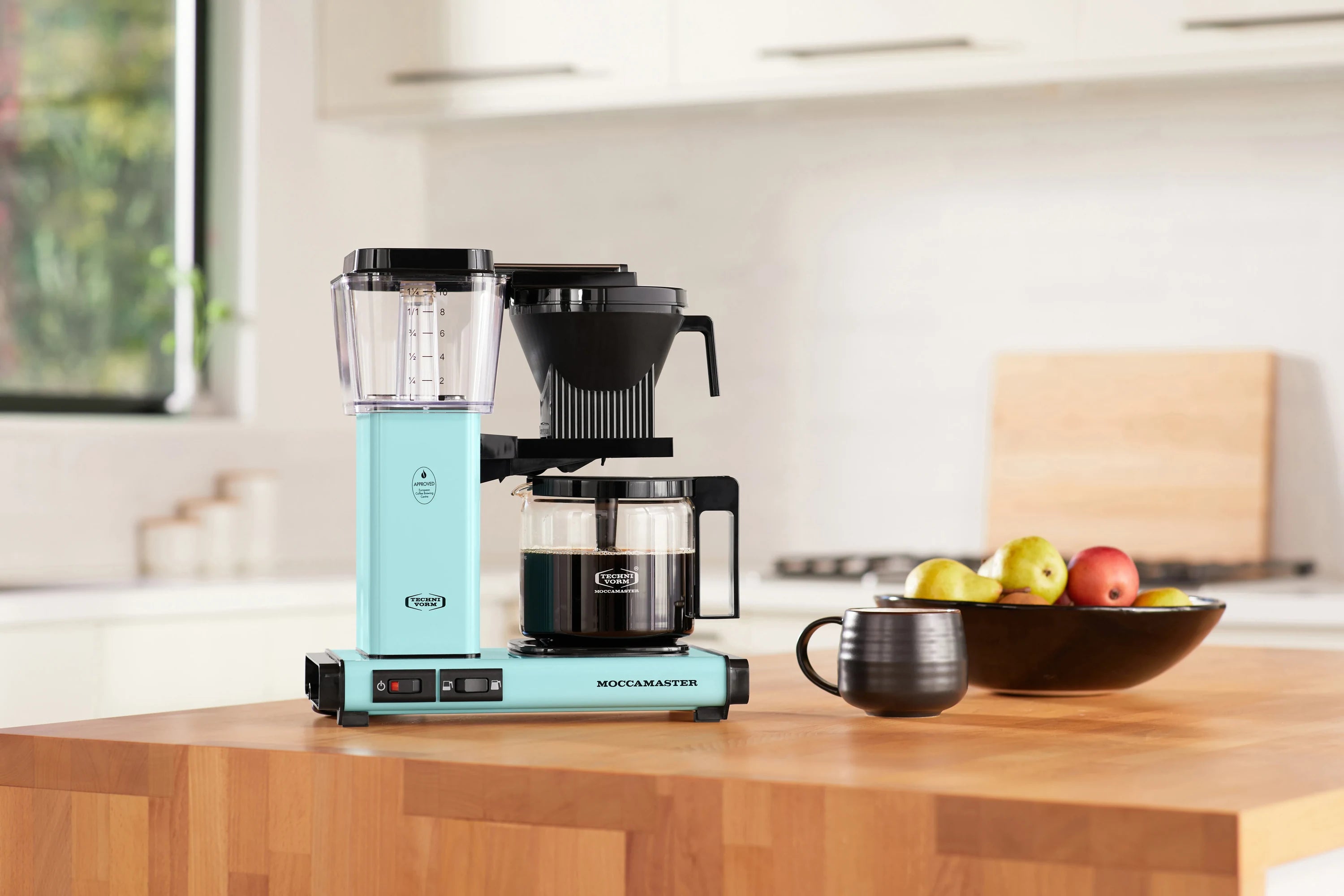 Turquoise coffee maker with glass carafe and clear water reservoir, black filter basket