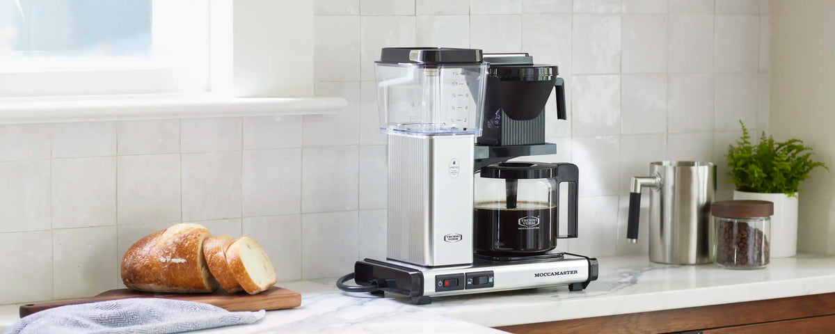 Moccamaster coffee maker with glass carafe and black brew funnel on kitchen counter.