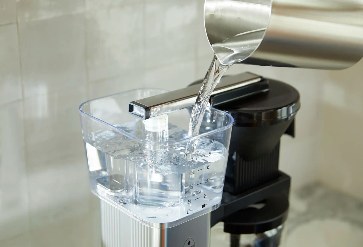 Moccamaster glass carafe with water pouring from polished silver spout onto black base