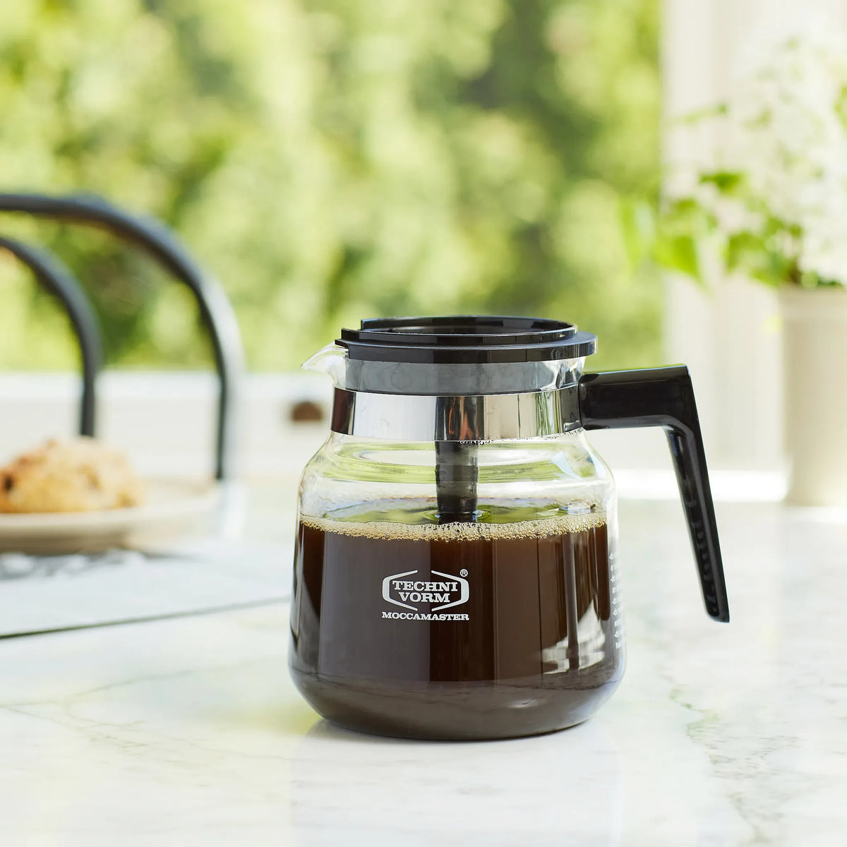 Glass coffee carafe with black handle and lid, brewed coffee level visible