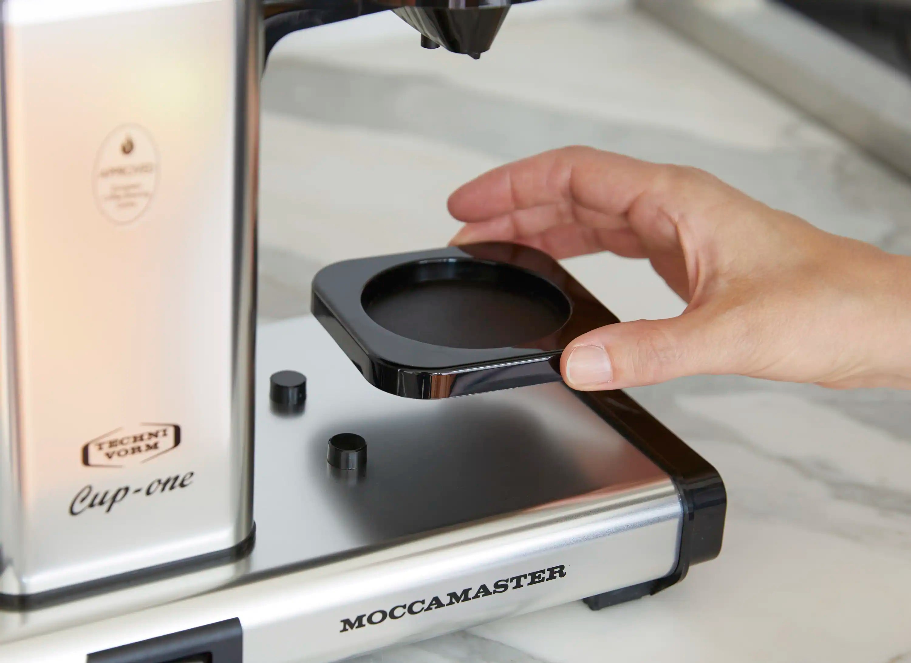 Single-cup coffee maker with black cup tray, hand adjusting the platform