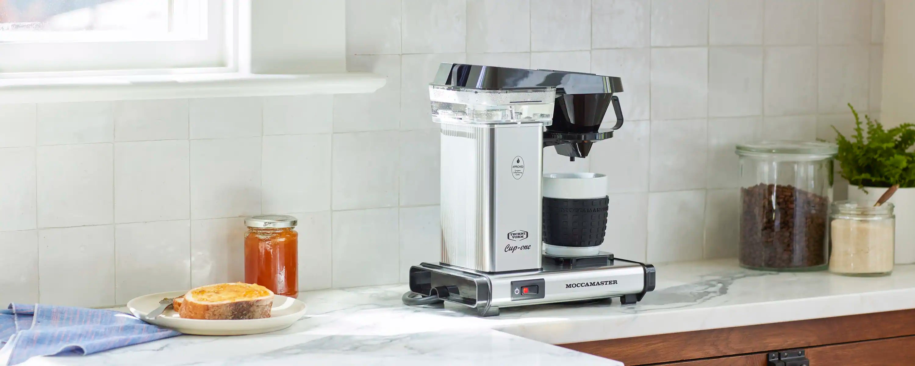Single-cup coffee maker in polished silver with black funnel on kitchen counter