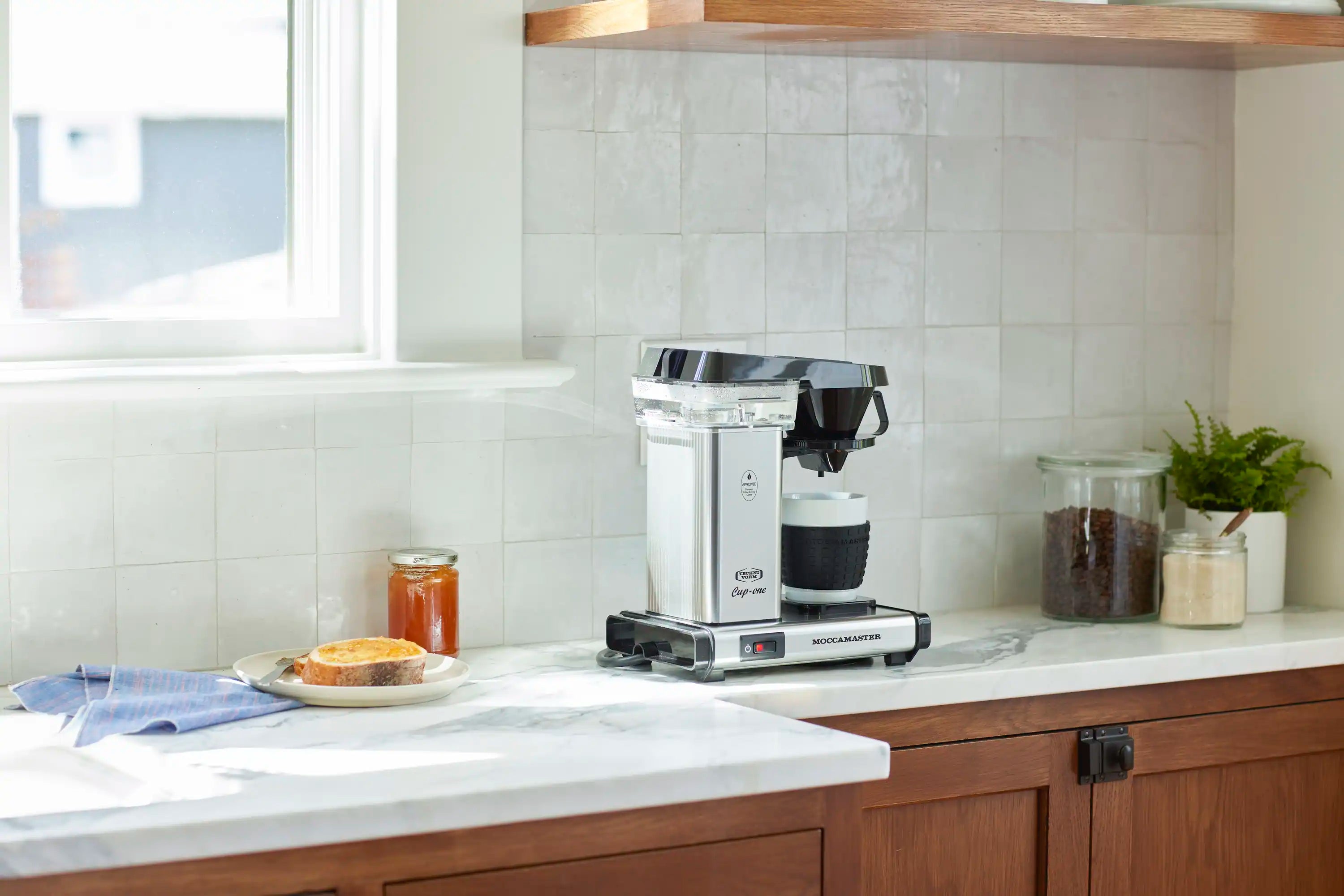 Single-cup coffee maker in polished silver with black funnel, front view on counter