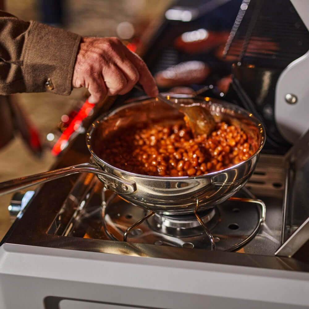 Stainless steel propane gas grill with pan on burner grate, cooking beans