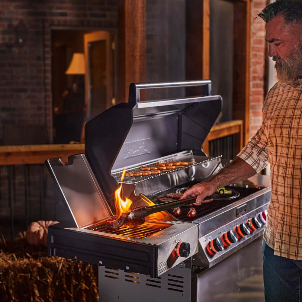 Stainless steel propane gas grill with open lid, flames at burners, cooking grates
