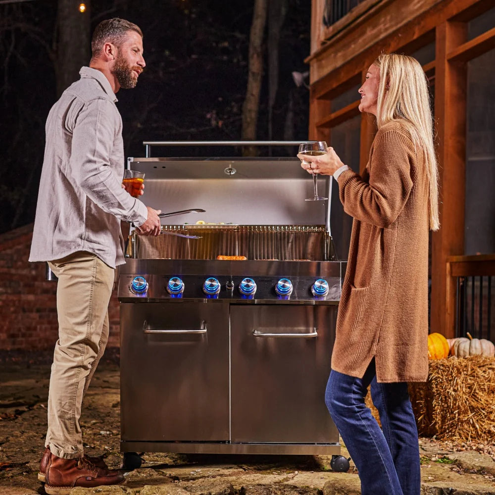 Two people using stainless propane grill with lid open and six blue burner knobs
