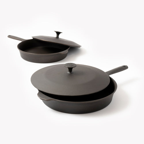 Two black cast iron skillets with lids and long handles