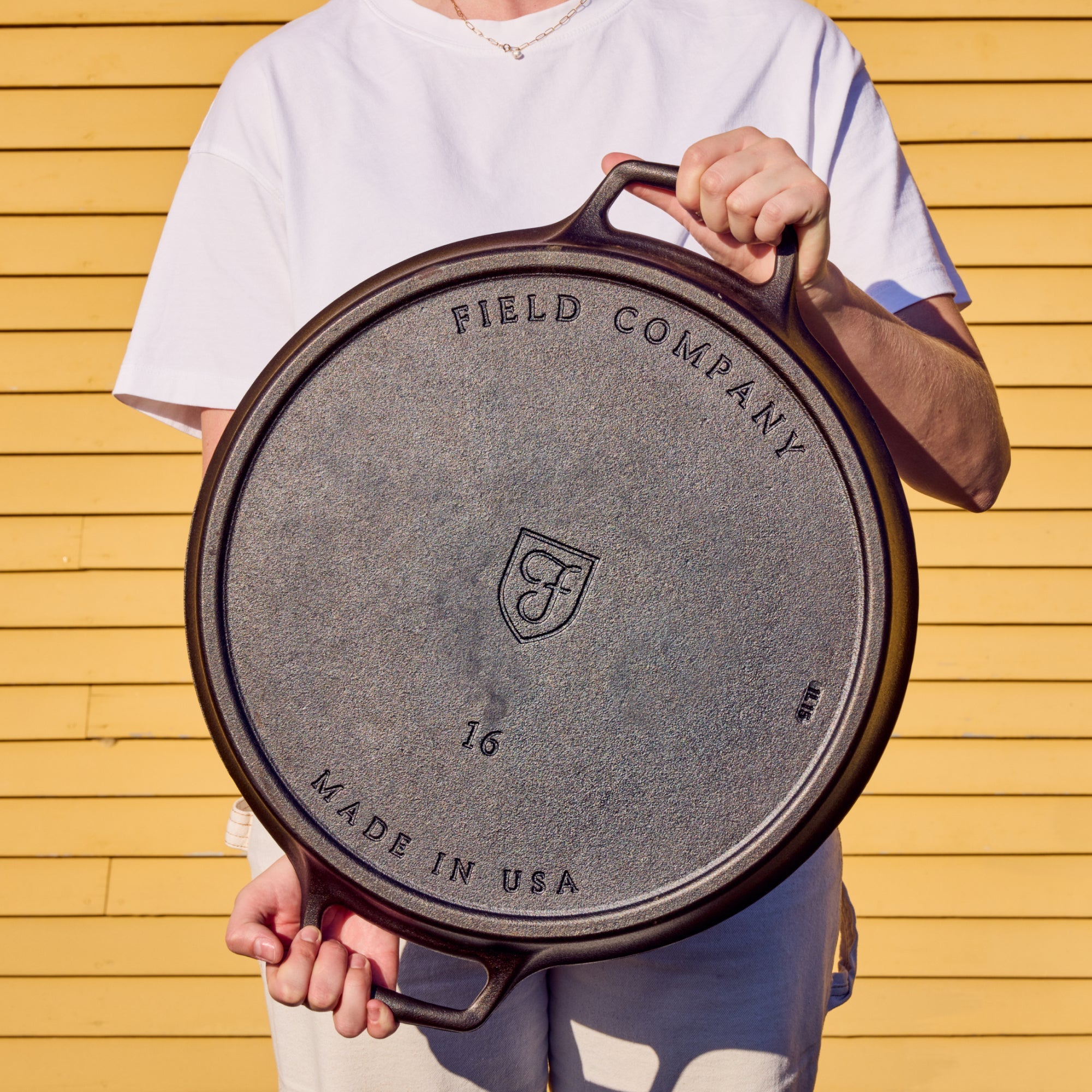 Field Company cast iron skillet held by a person, showing underside logo and text