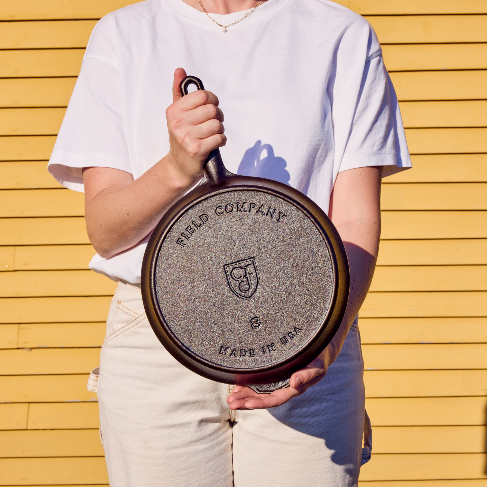 Field Company cast iron skillet held by a person in front of a yellow wall
