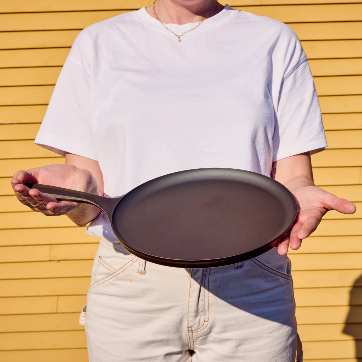Round cast iron griddle held horizontally with dark cooking surface