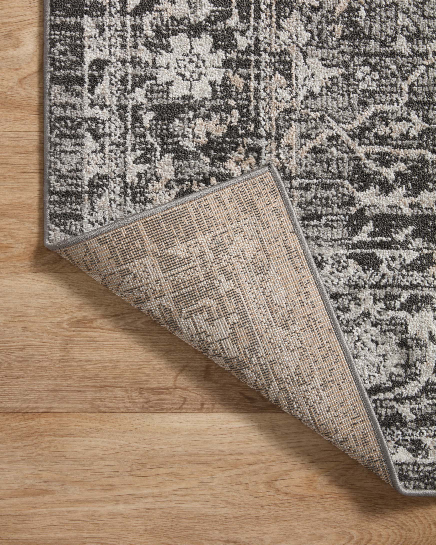 Charcoal and silver traditional area rug edge with woven texture, rolled for display.