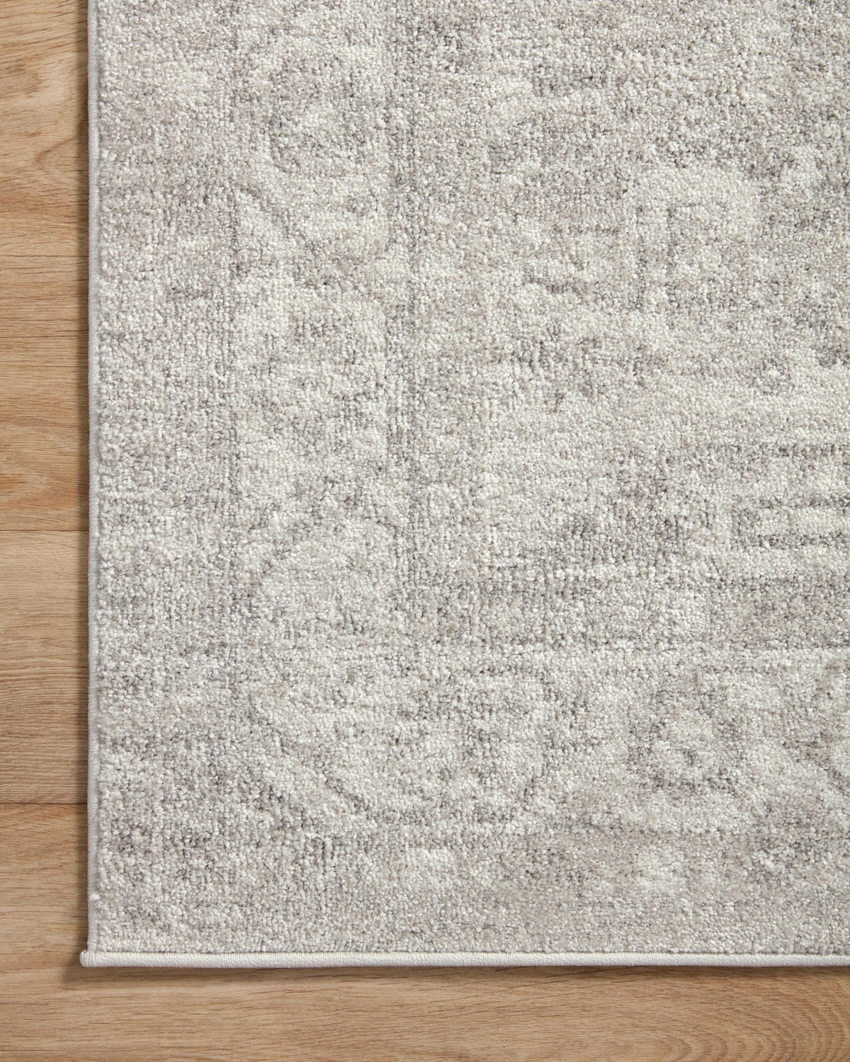 Traditional area rug in light silver and ivory with stitched border and mottled distressed texture