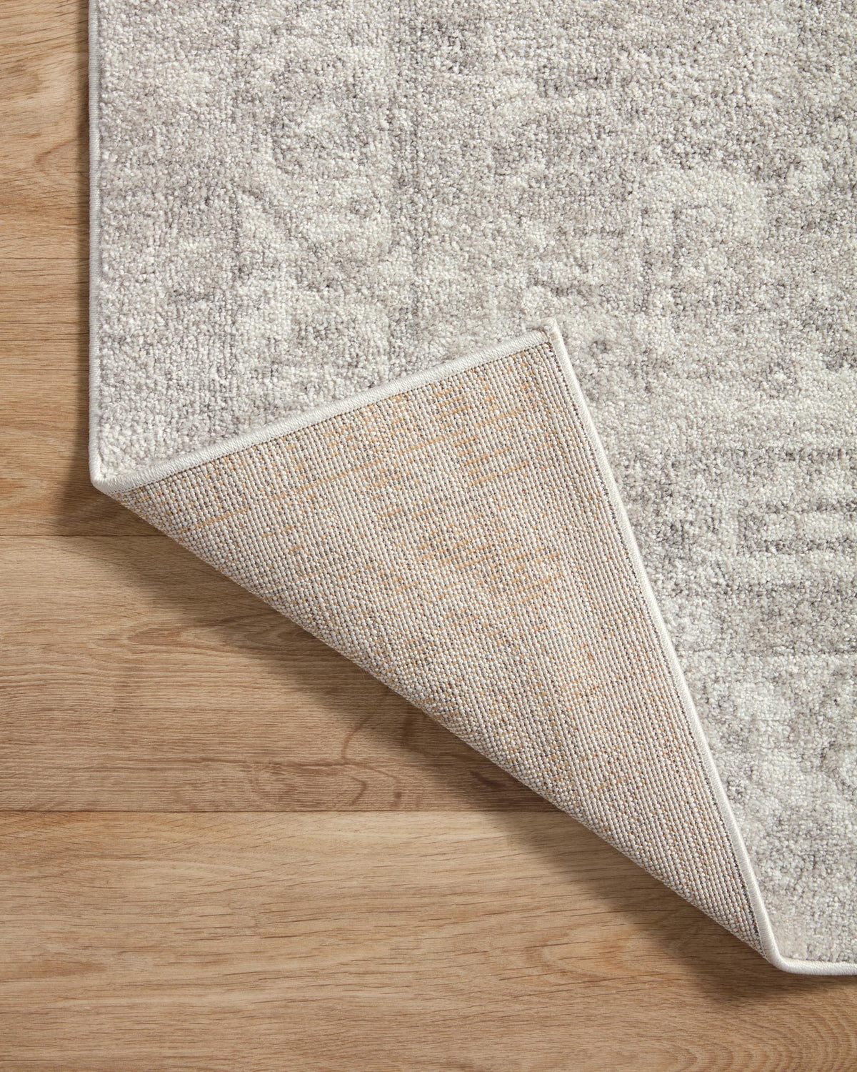 Ivory and silver rug showing woven underside and angled edge on wood floor