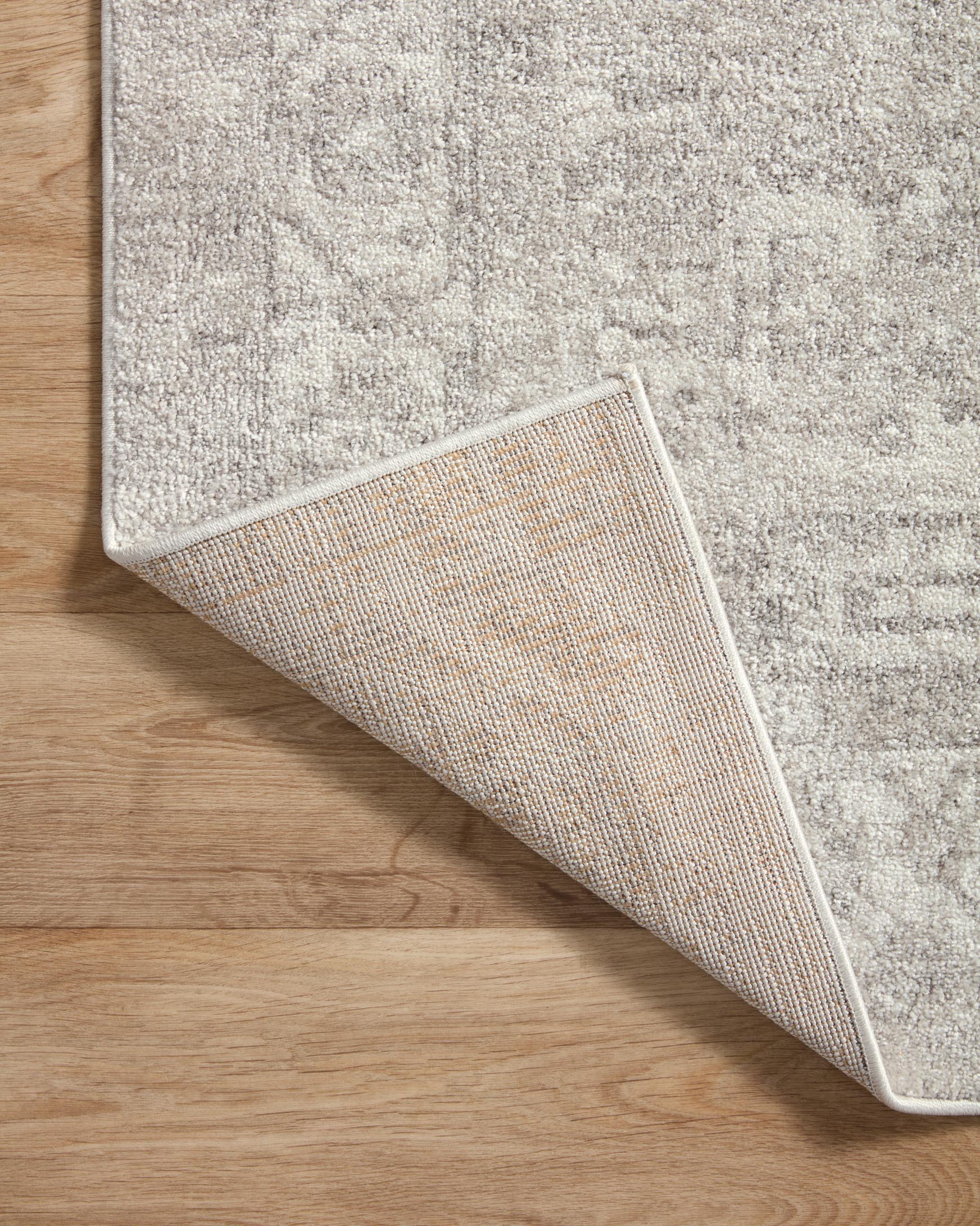 Traditional area rug folded corner showing woven underside and silver-gray ivory surface.
