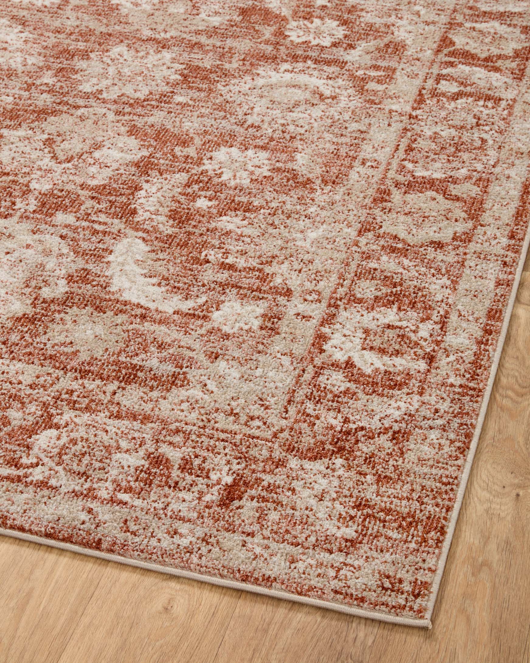 Rust and ivory traditional area rug flat on hardwood floor with distressed central motif