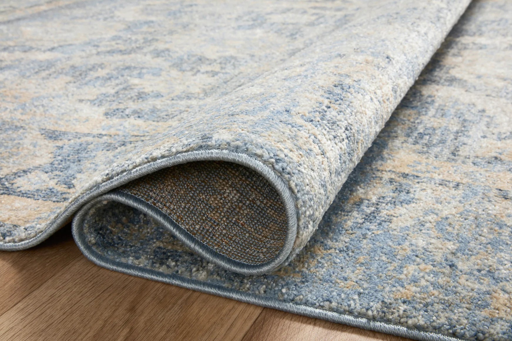 Sky and beige traditional area rug edge detail, distressed weave texture and dark bound trim