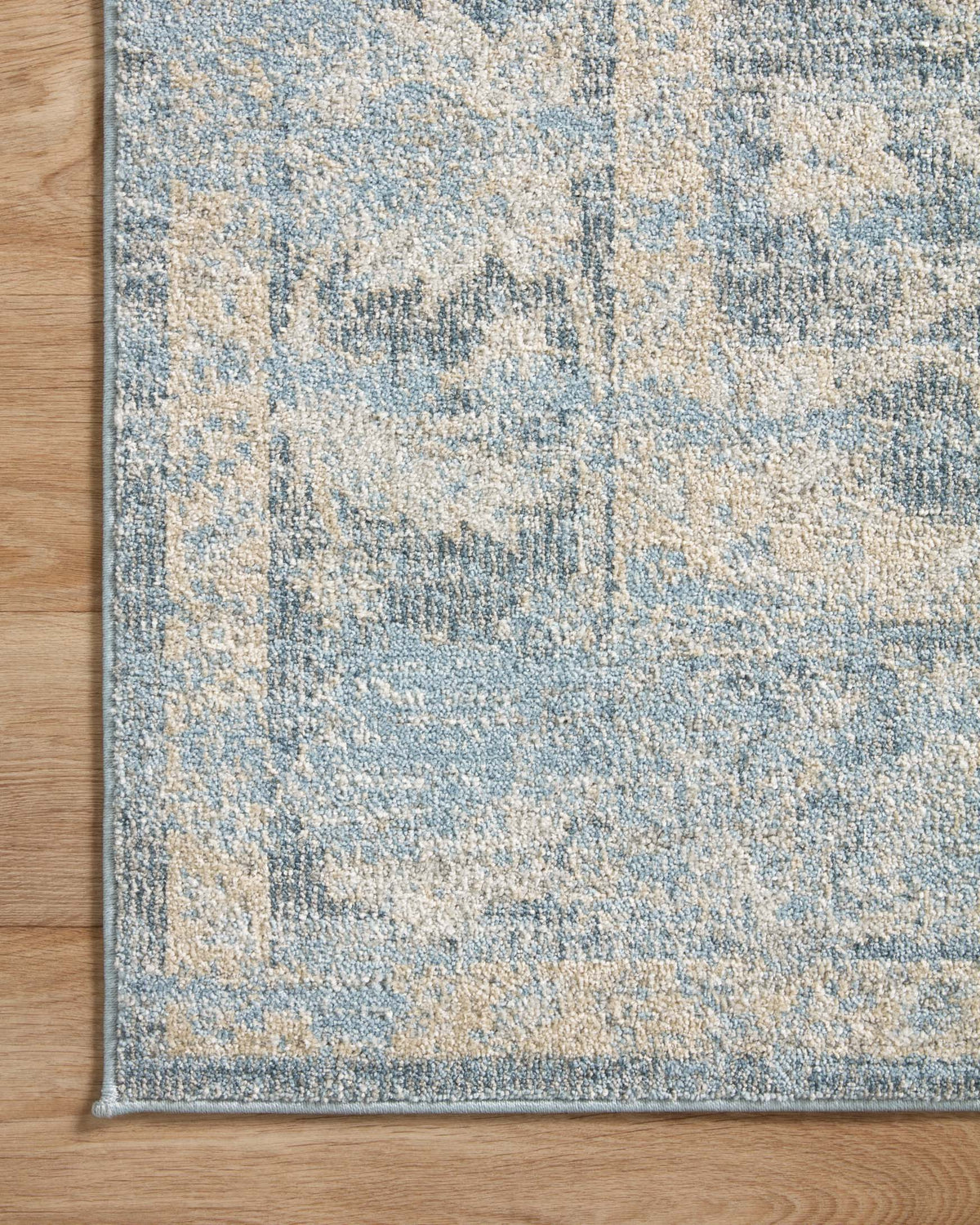 Blue and beige area rug corner with patterned field and thin border