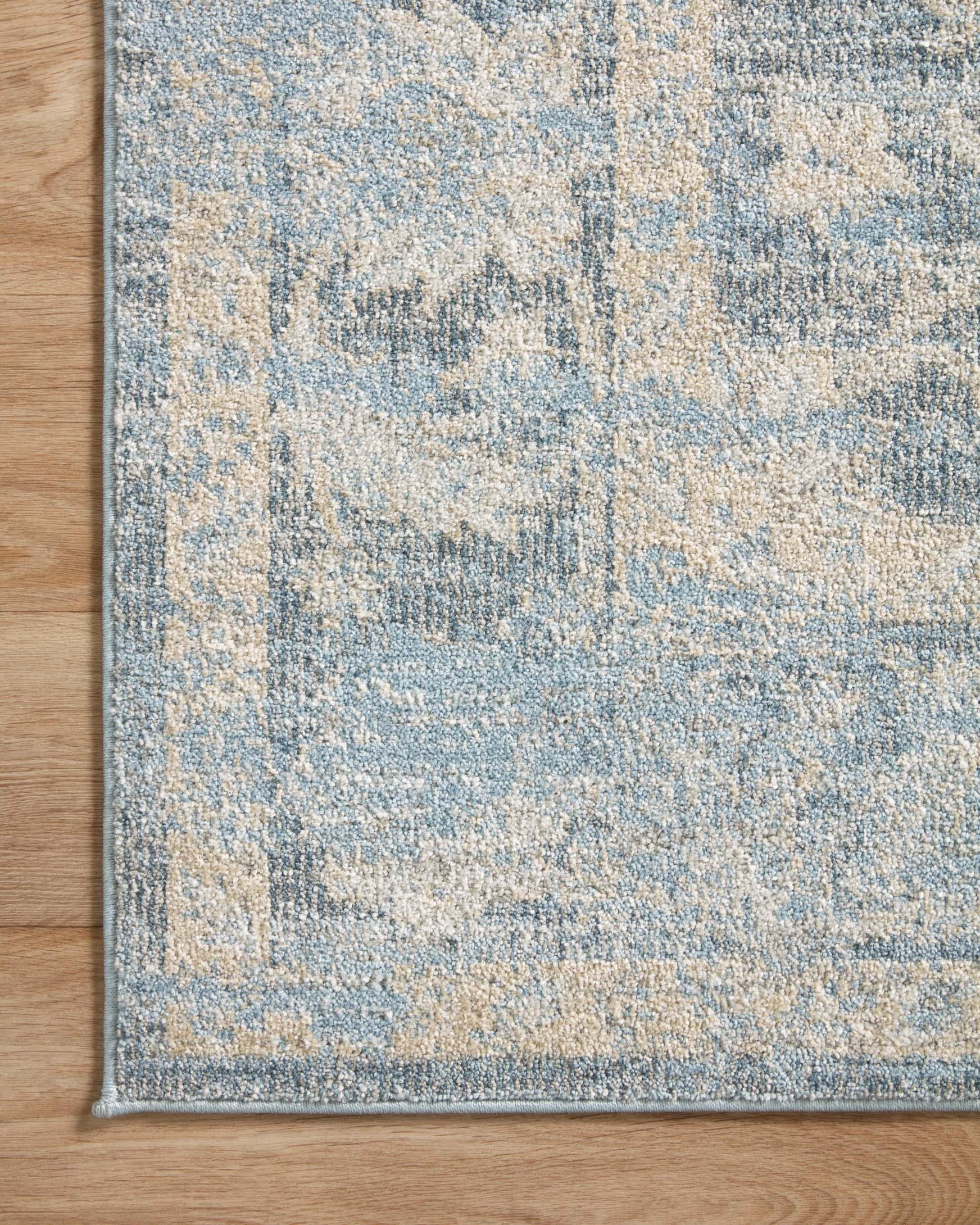 Sky and beige traditional area rug corner with dark border trim and faded distressed pattern